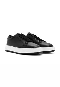 Baskets en cuir noir au toucher lisse, avec une semelle en caoutchouc blanc et des lacets noirs, bout rond et design minimaliste.