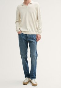 Krämfärgad långärmad tröja med krage, kombinerad med blå denimjeans och vita sneakers. Tröjan har en avslappnad passform och ribbade mudd.