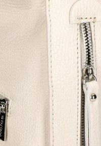 Krémová kožená taška s texturovaným povrchem, stříbrným zipem a precizním prošíváním. Obsahuje poutko zipu a drobný kovový akcent.