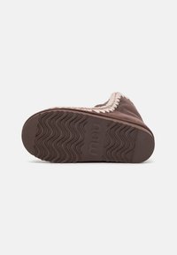 Pantofola in suede marrone con suola in gomma texturizzata, caratterizzata da un bordo di colore chiaro in contrasto lungo il bordo e un sottile motivo a onde sulla suola.