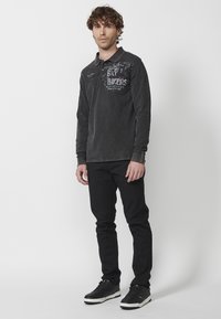 Ciemnoszara koszulka polo z długim rękawem, z czerwonymi akcentami kołnierzyka, z graficznym tekstem i wzorami. W komplecie ze slim-fit czarnymi spodniami i sneakersami.