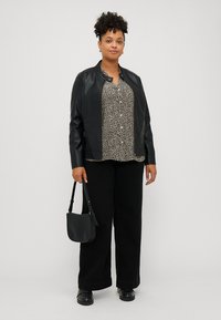 Veste en cuir synthétique noire avec un col rond, haut à motifs en noir et beige, pantalon décontracté noir et petit sac à main noir.
