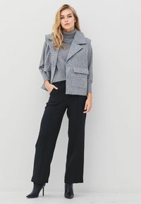 Gray sleeveless vest with studded accents over a fitted gray turtleneck, paired with black wide-leg pants and black heeled boots.