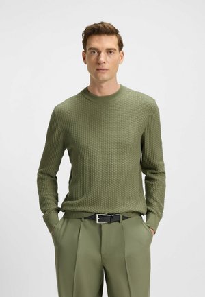 Grüner gestrickter Pullover mit einem strukturierten Muster, Rundhalsausschnitt und langen Ärmeln, kombiniert mit passenden grünen Hosen und einem schwarzen Gürtel.