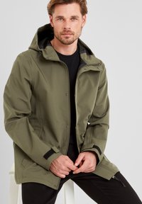 Olive green, hooded jacket with a zip closure, adjustable cuffs, and a smooth texture. Layered over a black shirt.