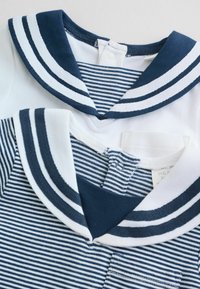 To marineblå og hvide stribede toppe med sømandshals, den ene ensfarvet hvid med marineblåt kantbånd, den anden marineblå og hvide striber med en frontlomme.