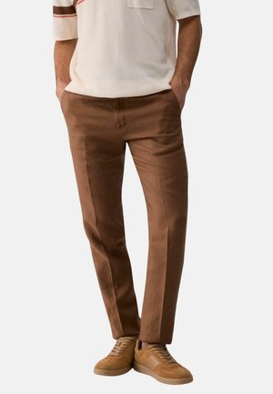 Uomo con pantaloni marroni slim fit con tasche laterali e sneakers in pelle scamosciata color cuoio con lacci.