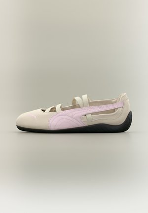 Ballerine beige et rose clair avec semelle noire, brides élastiques sur le dessus et logo Puma près des orteils.