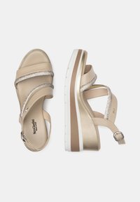 Sandales compensées beiges avec des accents métalliques, une sangle ajustable et deux brides pailletées sur le dessus. Semelle blanche et beige pour un bon maintien.