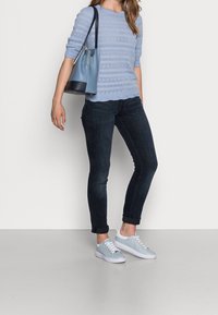 Maglione azzurro chiaro a maglia con maniche corte, jeans blu scuro e sneakers azzurro chiaro, abbinati a una borsa azzurro chiaro e navy.