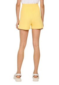 Geel badstof shorts met een elastische tailleband, met een relaxte pasvorm en een lengte boven de knie, gecombineerd met witte sandalen.