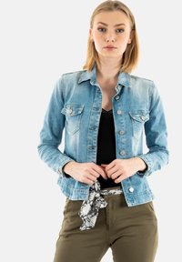 Ljusblå denimjacka med långa ärmar, två bröstfickor och silverfärgade knappar. Kombinerad med en svart topp och olivgröna byxor.