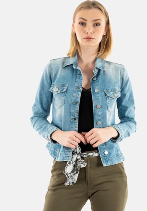 Light blue denim jacket with long sleeves, two chest pockets, and silver buttons. Paired with a black top and olive green pants.