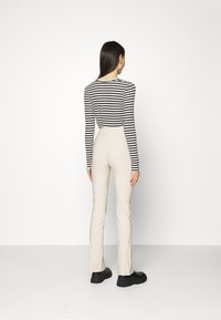 Černobíle pruhovaný top s dlouhým rukávem, který se kombinuje s béžovými úzkými kalhotami a černými botami. Hladká tkanina a šitý design zdůrazňují elegantní siluetu.