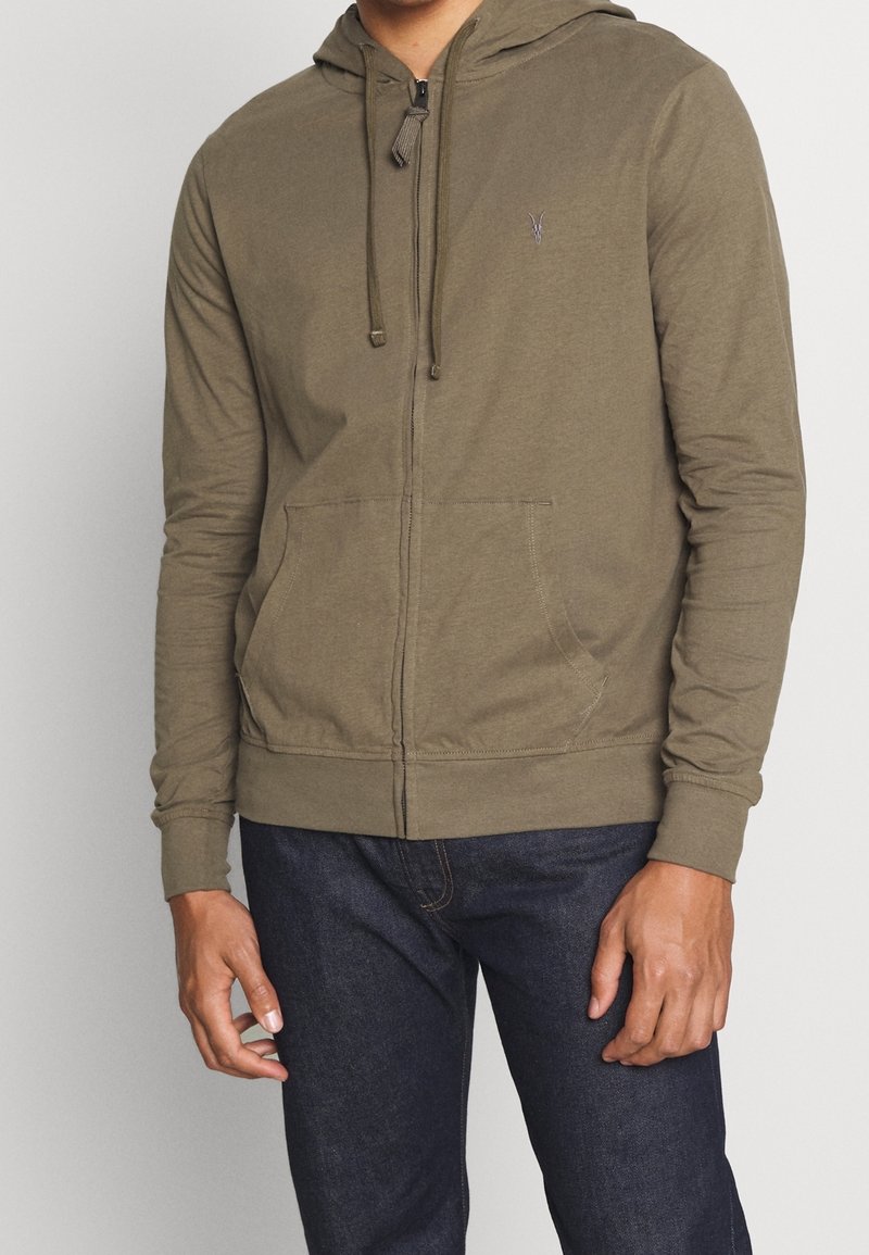 Sudadera con capucha y cremallera de color verde oliva, fabricada con tela suave, con bolsillo tipo canguro, capucha ajustable con cordón y puños acanalados. Diseño sencillo.