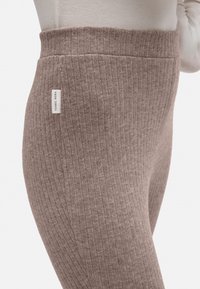 Leggings de rayas marrones con una cintura alta. Hechos de una tela suave, con una pequeña etiqueta en el lateral. Textura suave y diseño ajustado.