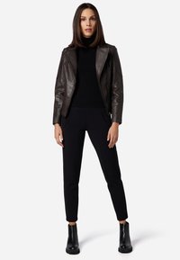 Braune Leder-Motorradjacke mit gerippten Schultern, schwarzer Rollkragenpullover und schwarzen maßgeschneiderten Hosen, ergänzt durch schwarze Ankle-Boots.