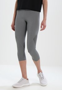 Leggings capri grigi realizzati in materiale elastico, con un accento in rete sul lato e abbinati a scarpe da tennis bianche.