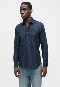Námornícky modrá košeľa na zapínanie s geometrickým vzorom, dlhými rukávmi a špicatým golierom. Vyrobená z hladkého materiálu s jemným leskom.
