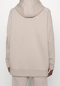 Sweat-shirt à capuche beige avec une coupe décontractée, doté d'une poche kangourou et de poignets côtelés. Tissu doux avec un design minimal et sans logos visibles.