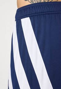 Navy urheilushortsit, joissa on valkoiset vinoraitat, valmistettu sileästä ja kevyestä kankaasta. Mukana joustava vyötärönauha mukavuutta varten.