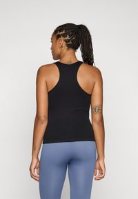 Svart atletisk tank topp med racerback-design, tettsittende fasong og glatt tekstur. Brukt sammen med lys blå ribbede tights.