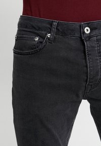 Jeans de mezclilla negra con corte recto, diseño de cinco bolsillos, botones metálicos y sutiles detalles desgastados en la parte delantera.