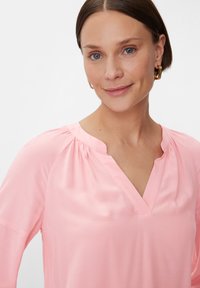 Rosa Bluse mit weicher Textur, mit V-Ausschnitt und gerafften Details an den Schultern. Einfaches, schlankes Design mit langen Ärmeln.
