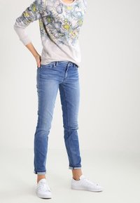 Felpa grigia chiara con motivo floreale, abbinata a jeans skinny blu chiaro e sneakers bianche. Texture liscia, vestibilità casual.