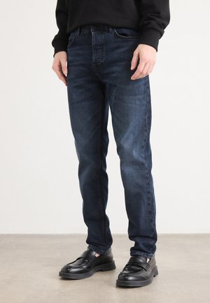 Dark blue denim jeans with a slim fit, featuring a classic five-pocket design and a subtle texture, paired with black loafers.