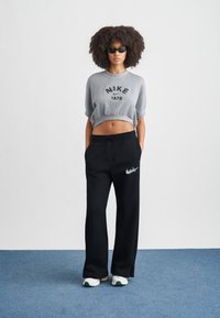 Sivo skrajšano majico s kapuco s črnim tiskom "Nike 1972", kombinirano s črnimi športnimi hlačami s srebrnim logotipom "Nike" in belimi supergami.