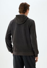 Mörkgrå huva med mjuk textur, ribbade ärmslut och fåll. Har raglanärmar och rundad nacke bak.