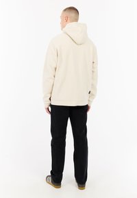 Beige hoodie met een buidelzak, capuchon en geribbelde manchetten, gecombineerd met zwarte rechte jeans en grijze schoenen met witte strepen.