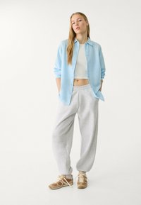 Light blue button-up shirt, white crop top, grey sweatpants, and brown sneakers. Smooth fabric, relaxed fit, casual style.