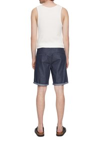 Débardeur blanc et shorts en denim foncé avec des ourlets roulés. Sandales avec une lanière sombre et une semelle brune contrastante. Vue de l'arrière.