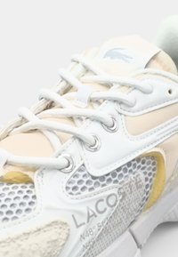 Baskets blanches avec dessus en mesh et cuir, présentant des accents pêche clair et gris, lacets ronds, œillets métalliques et logo imprimé.