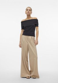 Svart av-shoulder topp med korte ermer, kombinert med høytlivede beige viddebukser; gulvlange, glatte stoffer og minimale folder.