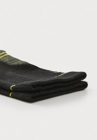 Calcetines negros de canalé doblados, con rayas verdes y amarillas en la parte superior. Textura suave con un diseño clásico adecuado para diversas ocasiones.