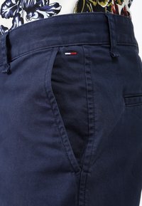 Námořnické modré bavlněné kraťasy s hladkou texturou, s bočními kapsami a malou červenou, bílou a modrou cedulkou na pase.