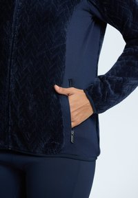 Marineblauwe ritsjack met een zachte, gestructureerde voorkant en gladde mouwen. Heeft zijzak met ritsdetail, ontworpen voor comfort en warmte.