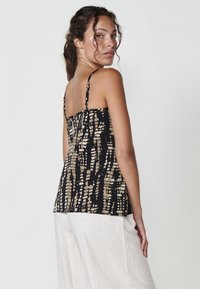 Zwart en goud-gepatroneerde mouwloze top met dunne bandjes, met een relaxed fit en textuurstof. De achterkant toont een geplooid ontwerp.