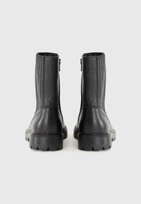 Botas de cuero negro hasta el tobillo con un acabado texturizado, que cuentan con paneles laterales elásticos, un zipper trasero y una suela robusta de tipo lug.