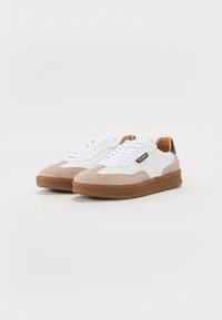 Sneaker con superiore in pelle bianca, punta in suede beige e suola in gomma color terra. Presenta lacci bianchi e un accento nera sul tallone con dettaglio del logo.