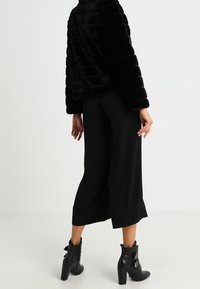 Veste en fausse fourrure noire avec des rayures horizontales, associée à un pantalon large noir et des bottines à boucles.