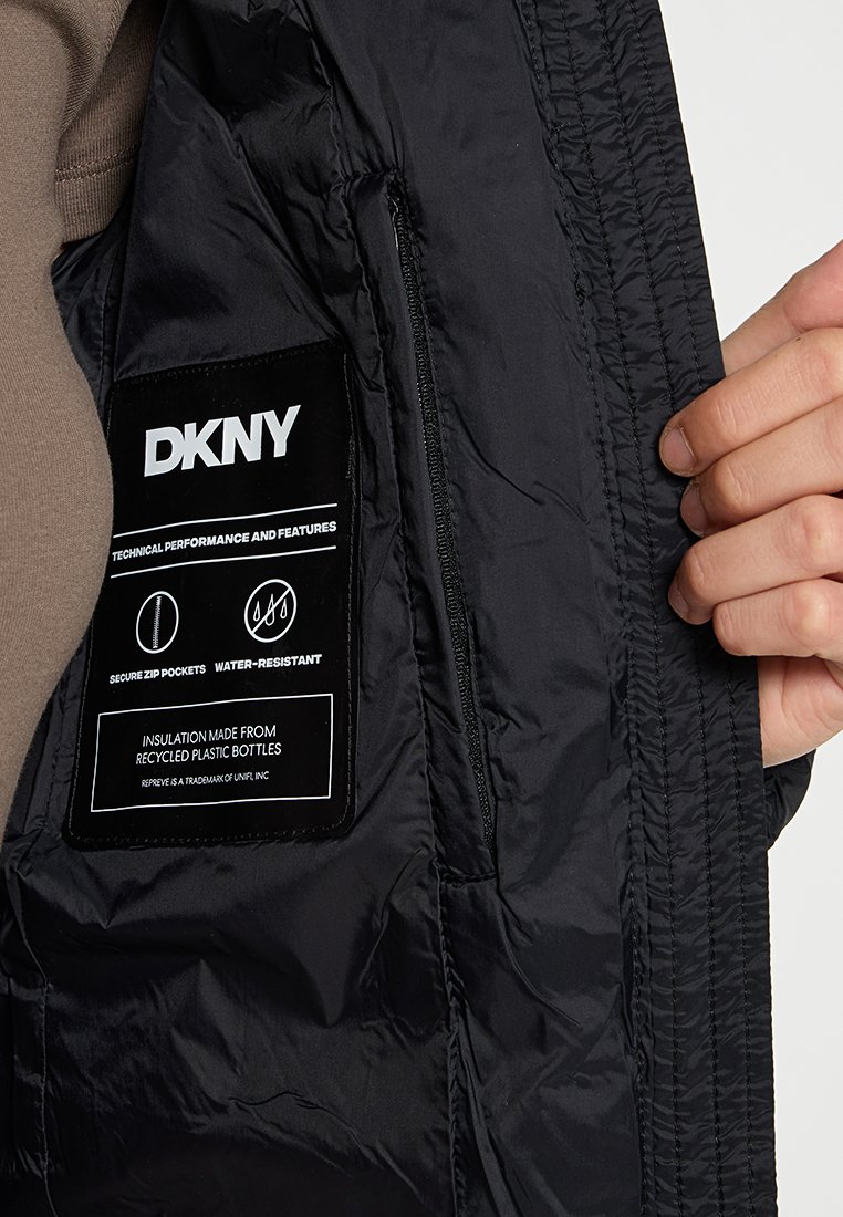 Interior de chaqueta acolchada negra con una etiqueta de tela. Cuenta con bolsillos con cremallera seguros y material resistente al agua. Aislamiento de botellas recicladas.