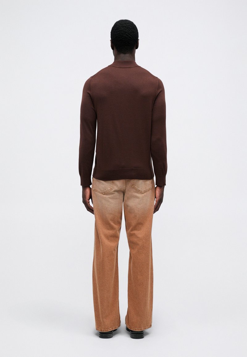 Brun striktrøje og lysebrune breddebenede jeans, begge med en glat struktur. Trøjen har en rund halsudskæring og ribbet manchetter.