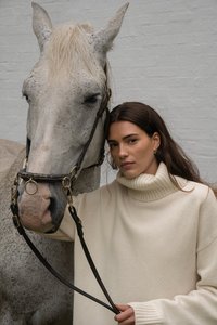 Gai krēms turtlenecks džemperis ar ribotām piedurknēm, apvienots ar pelēnu zirgu, kam ir melna ādas piestiprināšanas josta un misiņa aparatūra.