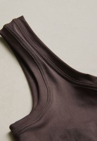 Gros plan d'un haut sans manches marron foncé montrant la bretelle d'épaule et les coutures détaillées sur fond beige.