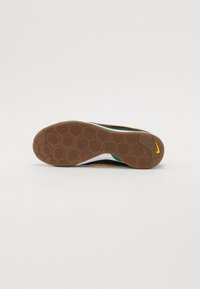 Hnedá gumová podrážka s hexagonálnym vzorom, biela medzipodrážka a čierny zvršok s žltými a zelenými akcentmi. Logo Nike viditeľné na päte.