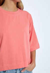 Korálově růžové oversized tričko s krátkými rukávy, kulatým výstřihem a jemnou bavlněnou texturou. Obsahuje rovný lem a subtilní šicí detaily.
